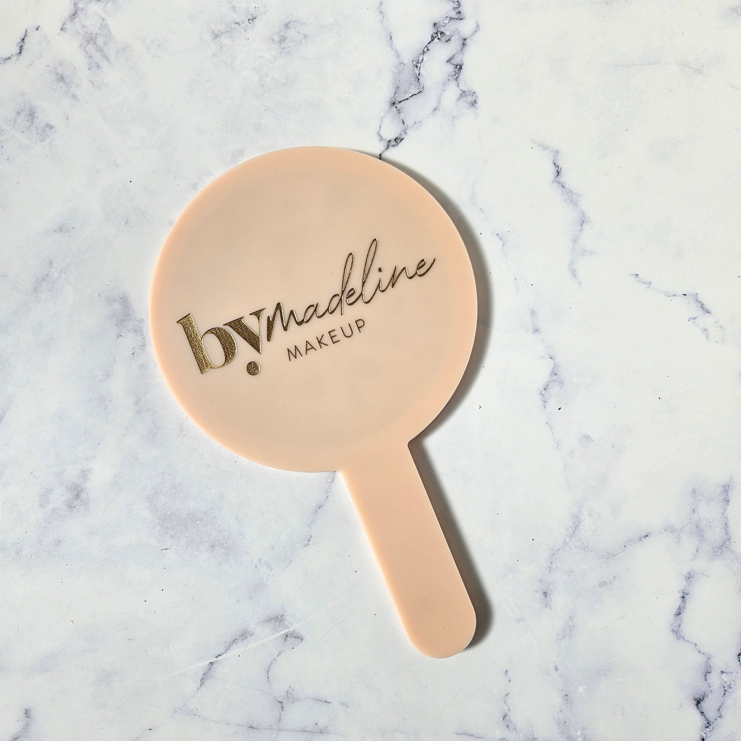 Round Handheld Mirror in Soft Peach Acrylic and Metallic Gold Logo